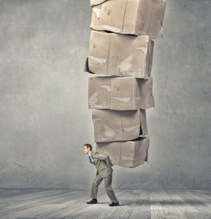 Young businessman in suit carrying big stack of carton boxes